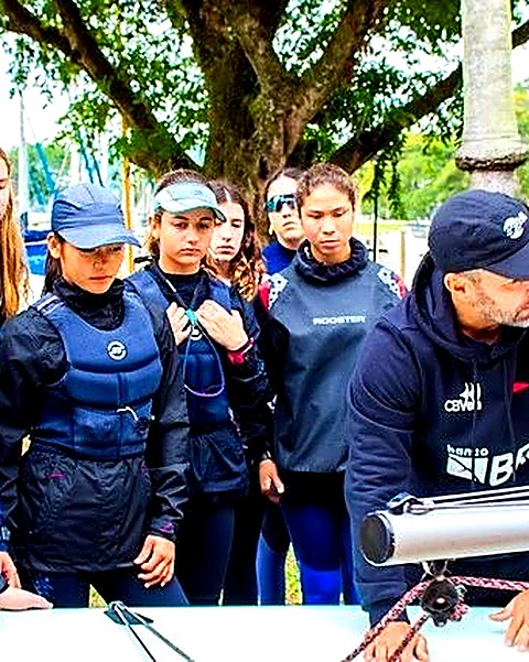 Crianças e jovens velejadores recebendo instrução à beira d'água